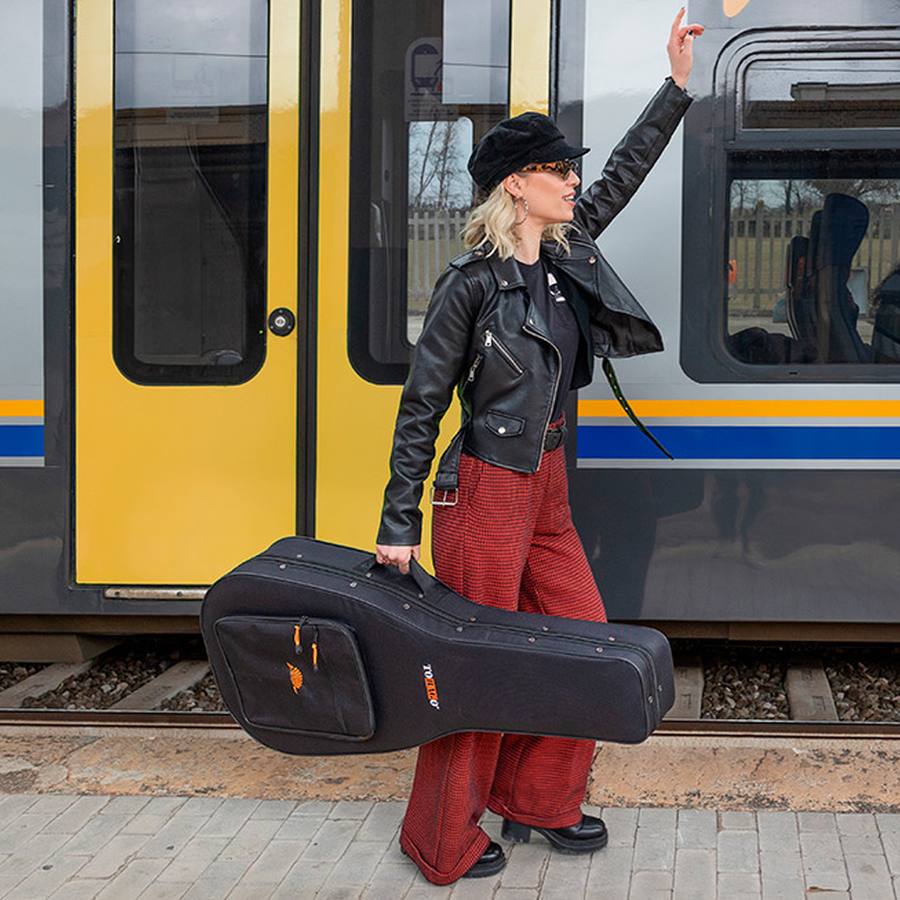 A guitar player traveling by train with their guitar in a TOBAGO semi-rigid case.