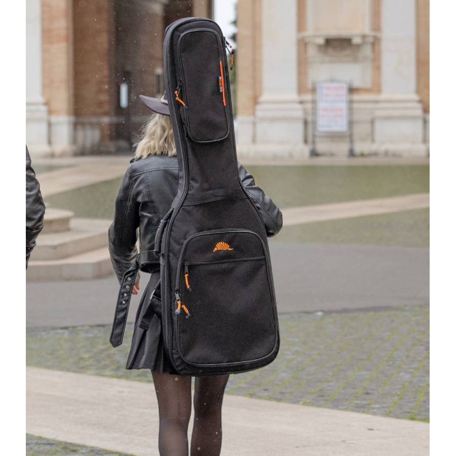 A bass player carrying their electric bass in a TOBAGO soft case, heading to perform at a concert in a square.